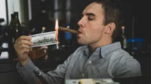 muž pálí bankovku a kouří z ní doutník