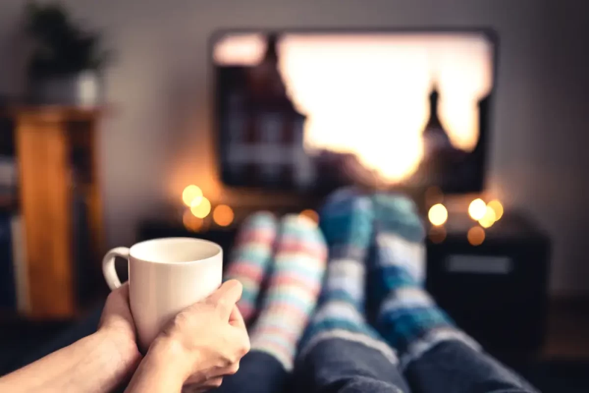 Lidé v ponožkách a hrnkem čaje sledují televizi