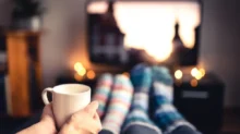 Lidé v ponožkách a hrnkem čaje sledují televizi