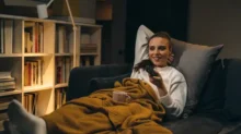 Žena pod dekou na gauči sleduje televizi