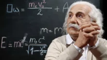 Albert Einstein, který sedí před tabulí.