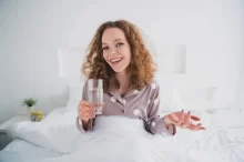 žena v posteli se sklenicí vody