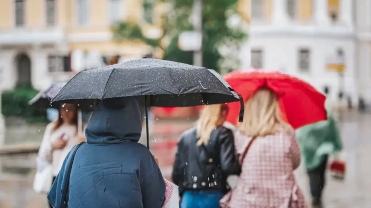 Lidé jdou po ulici schovaní pod deštníkem