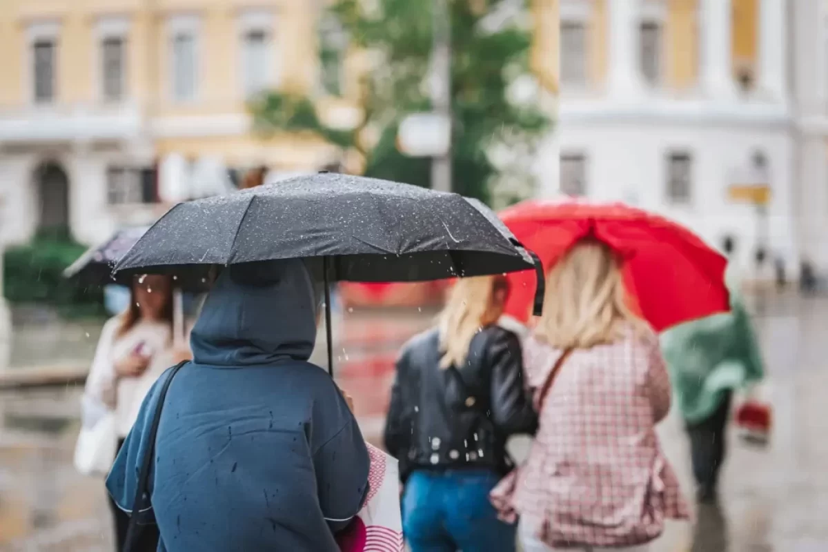 Lidé jdou po ulici schovaní pod deštníkem