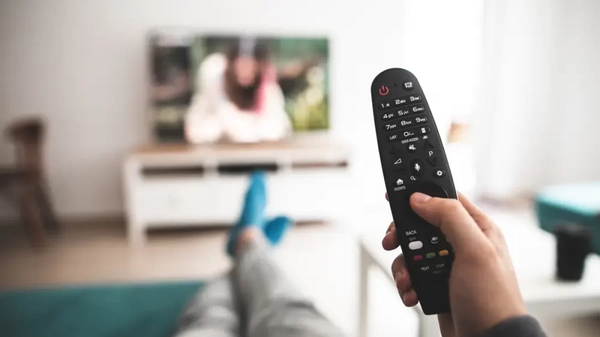 Člověk drží v ruce ovladač a dívá se na televizi