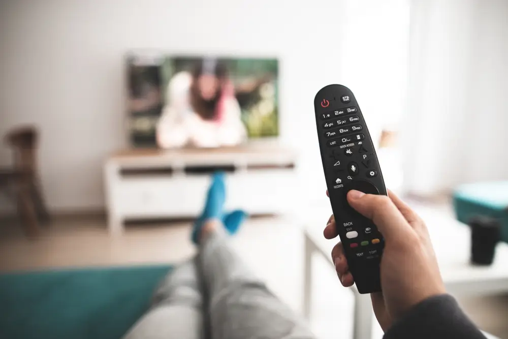 Člověk drží v ruce ovladač a dívá se na televizi