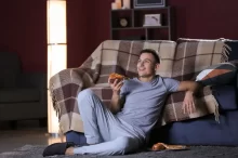 Muž se v noci dívá na televizi a jí u toho pizzu