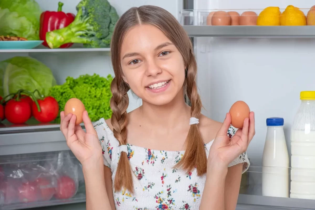 Dívka u lednice drží v ruce vajíčka