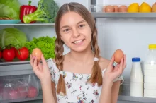 Dívka u lednice drží v ruce vajíčka