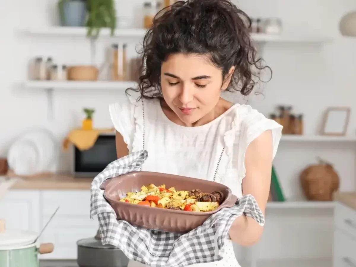 Žena drží v rukou pečící mísu s bramborami