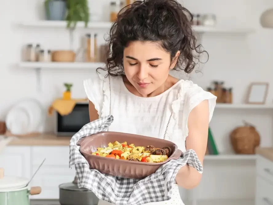 Žena drží v rukou pečící mísu s bramborami