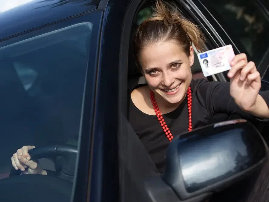 Spokojená žena za volantem ukazující řidičák