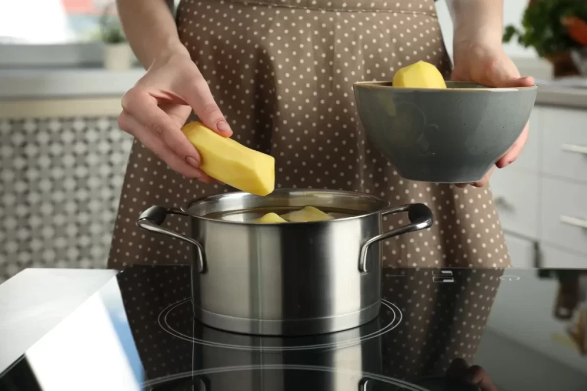 Žena dává brambory do hrnce