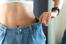 žena zhubla v pase, drží si kalhoty a ukazuje ploché břicho