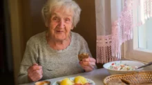Seniorka sedí u stoly s obědem