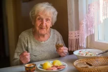 Seniorka sedí u stoly s obědem