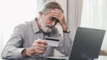 Důchodce se drží za hlavu s kreditkou v ruce u laptopu