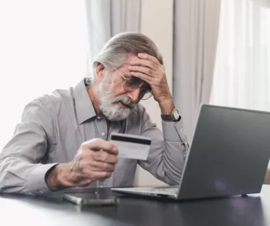 Důchodce se drží za hlavu s kreditkou v ruce u laptopu