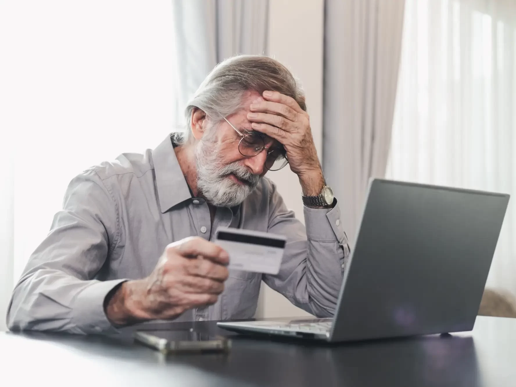 Důchodce se drží za hlavu s kreditkou v ruce u laptopu