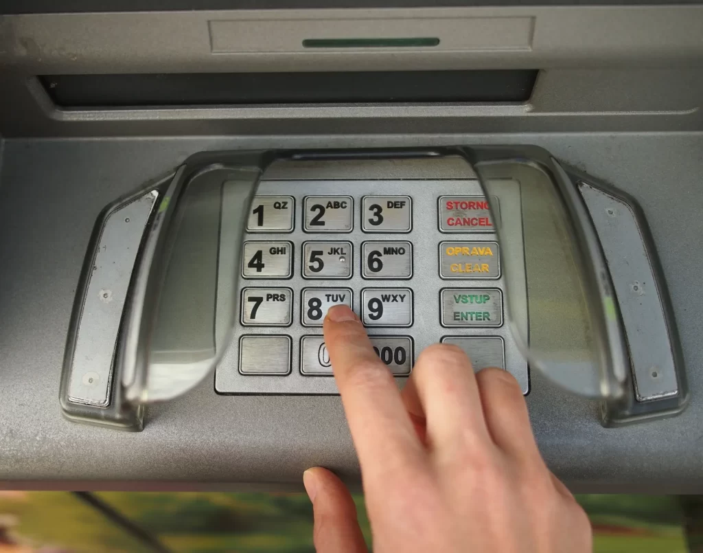 atm3 - Techsvět Detailní pohled na klávesnici bankomatu během zadávání PIN kódu. Prst osoby mačká číslo 8.