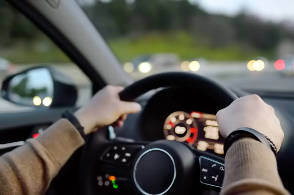 auto2 - Techsvět Pohled z perspektivy řidiče na ruce držící volant moderního automobilu.