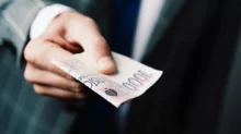 Muž v obleku podává bankovky v celkové hodnotě 3 000 Kč.