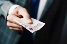 Muž v obleku podává bankovky v celkové hodnotě 3 000 Kč.