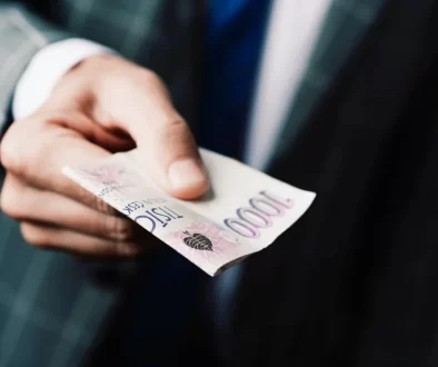 Muž v obleku podává bankovky v celkové hodnotě 3 000 Kč.