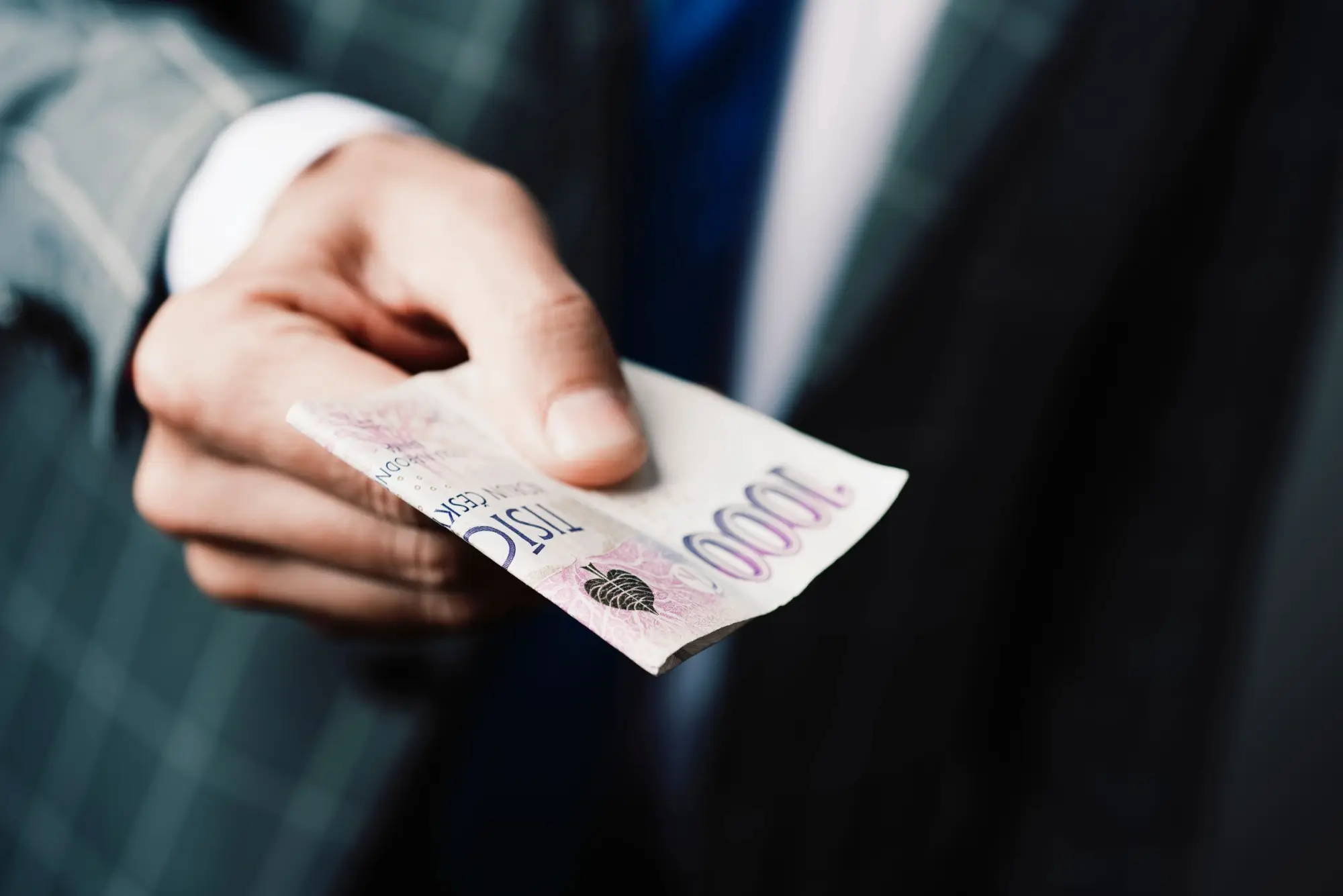 Muž v obleku podává bankovky v celkové hodnotě 3 000 Kč.