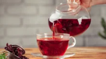 Skleněná konvice, ze které se nalévá žena sytě červený čaj do průhledného šálku.