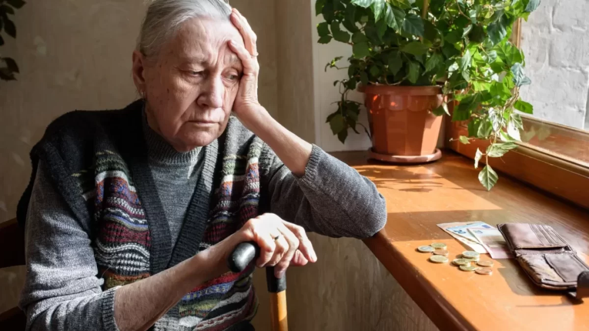 Stará žena sedí u okna a dívá se na peníze na parapetu