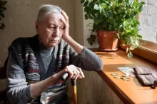 Stará žena sedí u okna a dívá se na peníze na parapetu