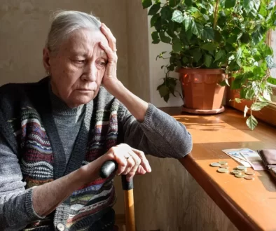 Stará žena sedí u okna a dívá se na peníze na parapetu