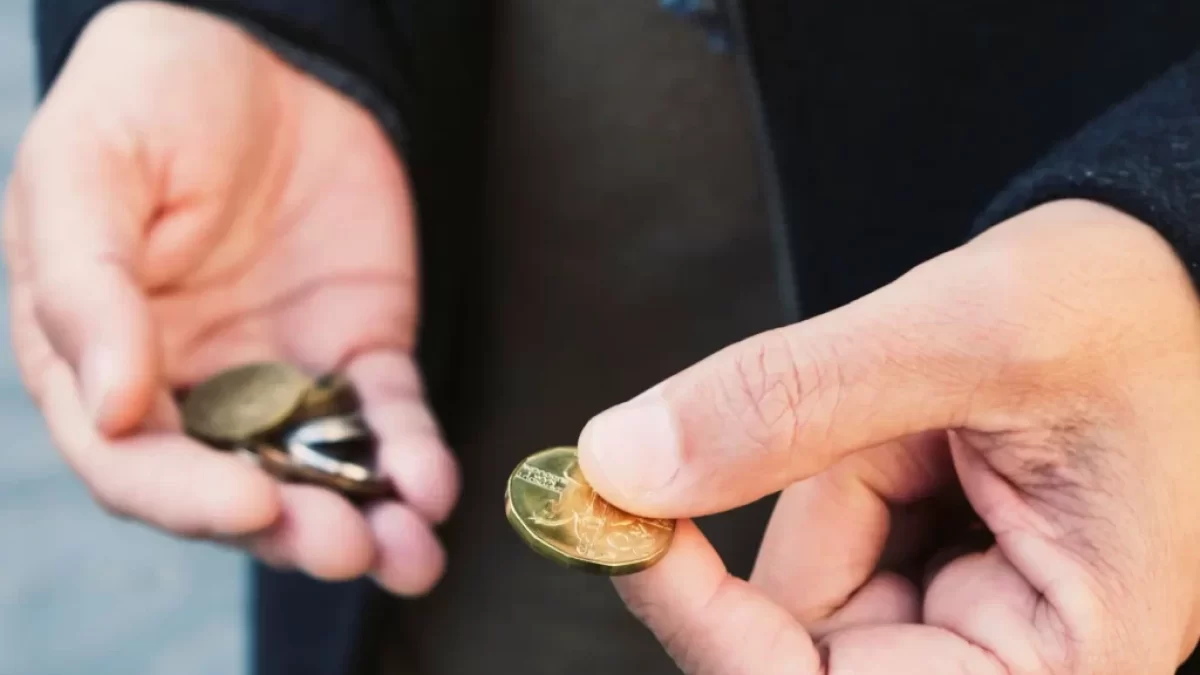 Ruce člověka, který drží drobné mince. V jedné ruce svírá hromádku mincí, zatímco druhou rukou vybírá jednu konkrétní.
