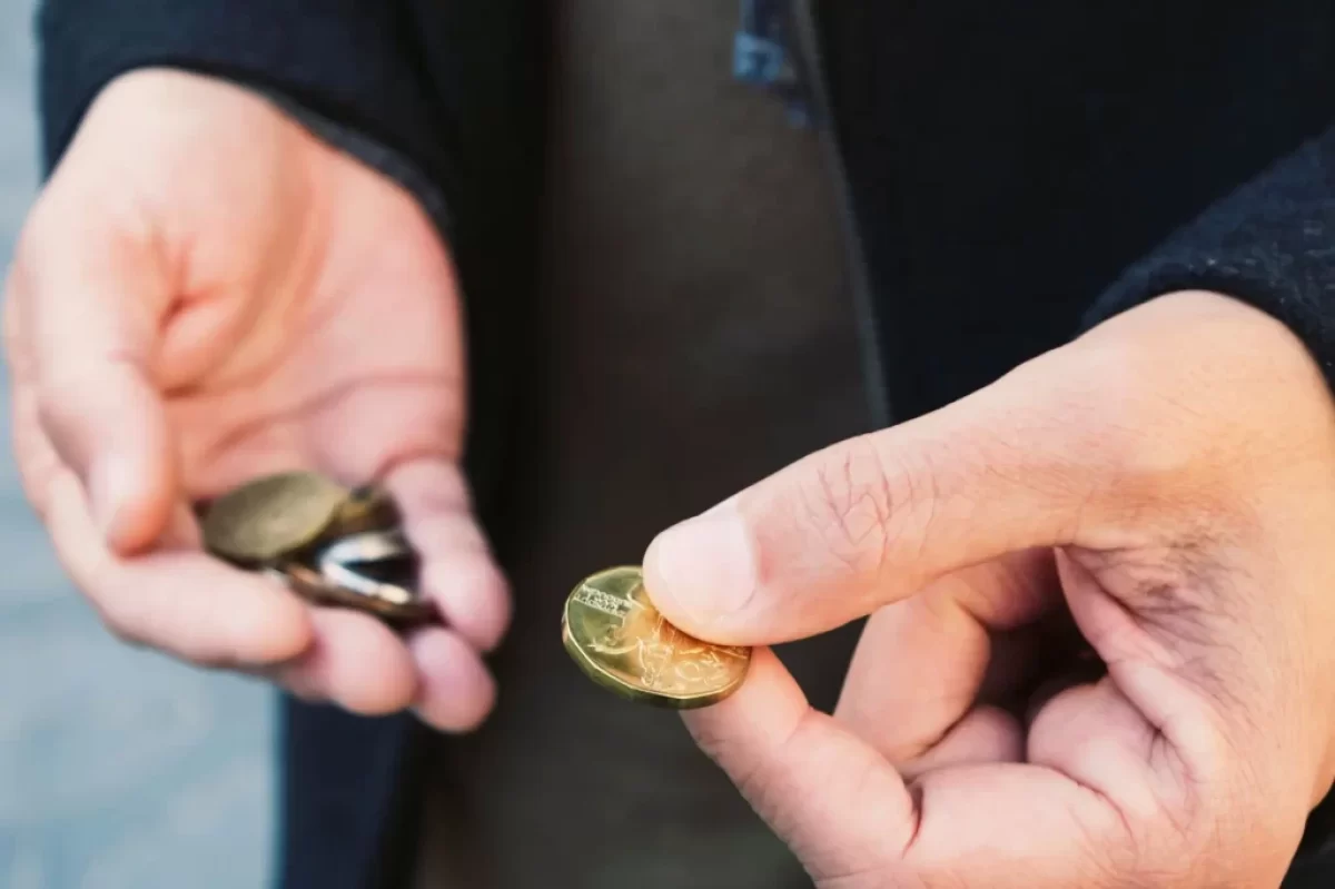 Ruce člověka, který drží drobné mince. V jedné ruce svírá hromádku mincí, zatímco druhou rukou vybírá jednu konkrétní.