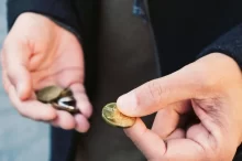 Ruce člověka, který drží drobné mince. V jedné ruce svírá hromádku mincí, zatímco druhou rukou vybírá jednu konkrétní.