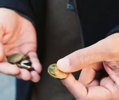 Ruce člověka, který drží drobné mince. V jedné ruce svírá hromádku mincí, zatímco druhou rukou vybírá jednu konkrétní.