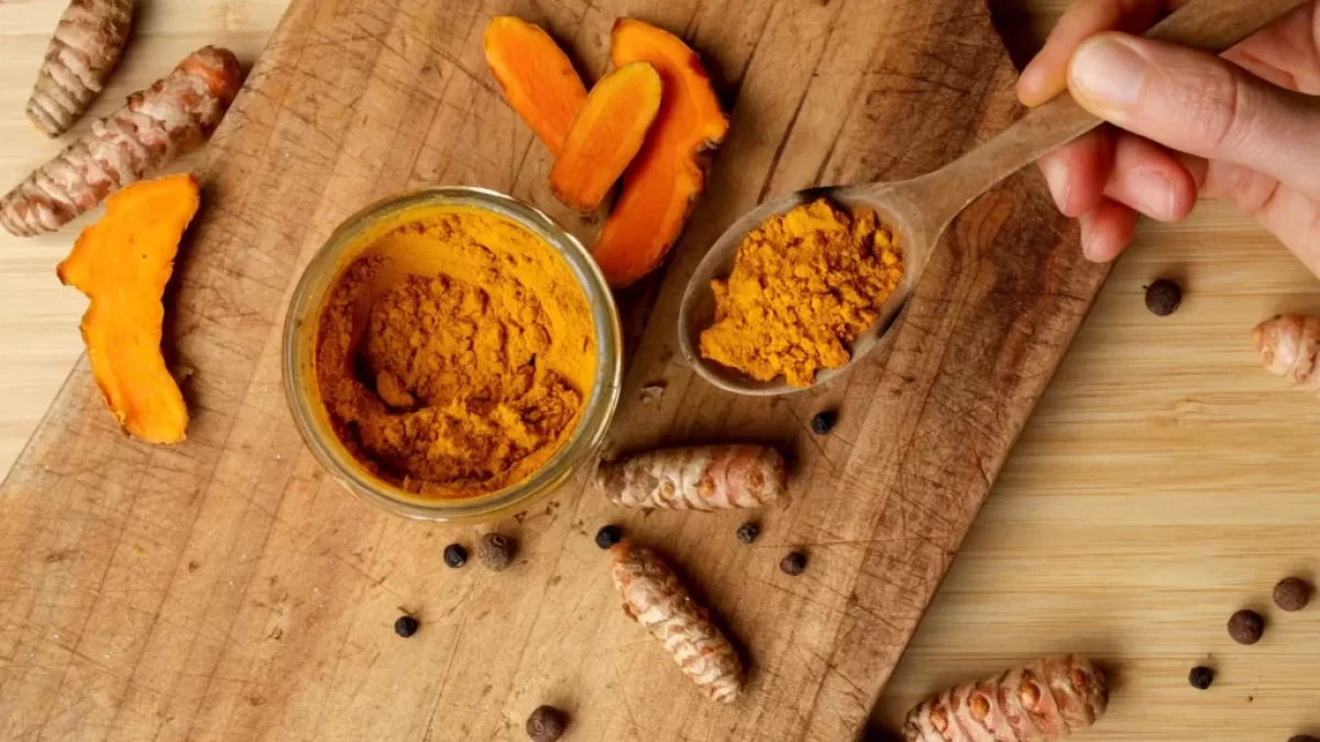 Žena drží dřevěnou lžíci mleté kurkumy