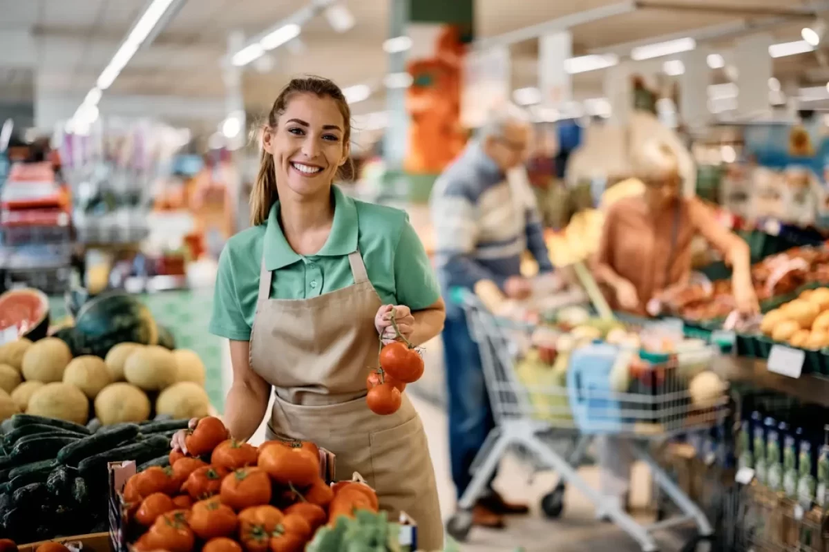 Prodavačka v supermarketu přerovnává rajčata.