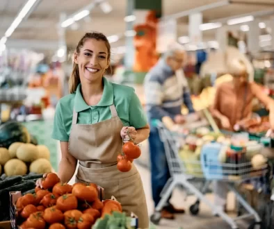 Prodavačka v supermarketu přerovnává rajčata.