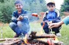 Dva chlapci opékají buřty na ohni u lesa