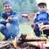 Dva chlapci opékají buřty na ohni u lesa