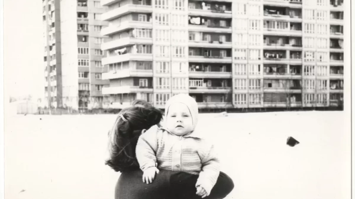 Retro fotografie - žena nese nemluvně, v pozadí panelový dům
