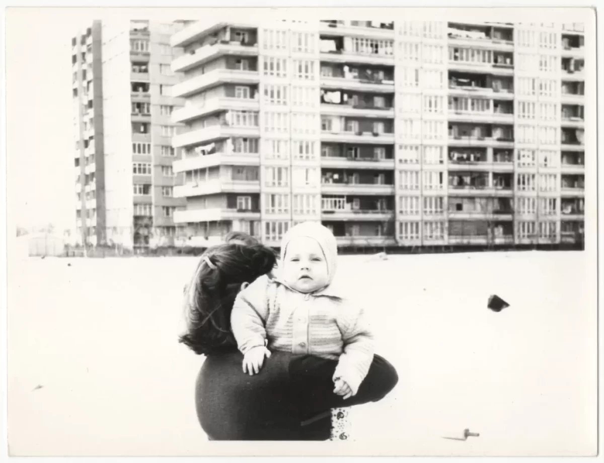 Retro fotografie - žena nese nemluvně, v pozadí panelový dům
