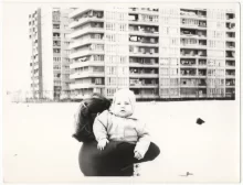 Retro fotografie - žena nese nemluvně, v pozadí panelový dům