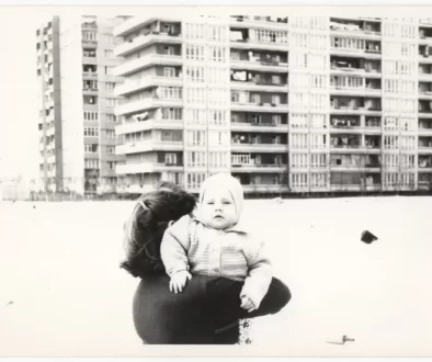 Retro fotografie - žena nese nemluvně, v pozadí panelový dům