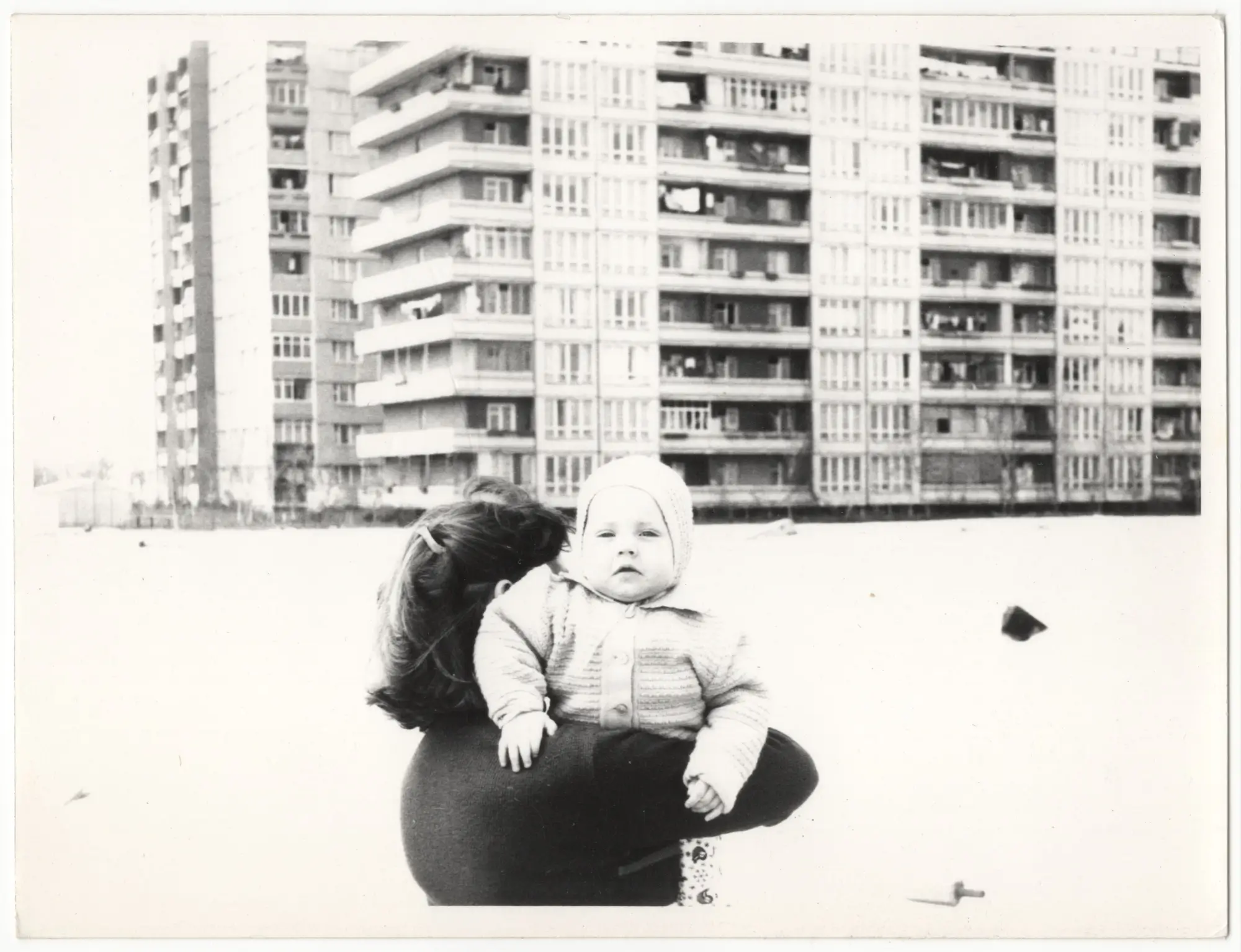 Retro fotografie - žena nese nemluvně, v pozadí panelový dům