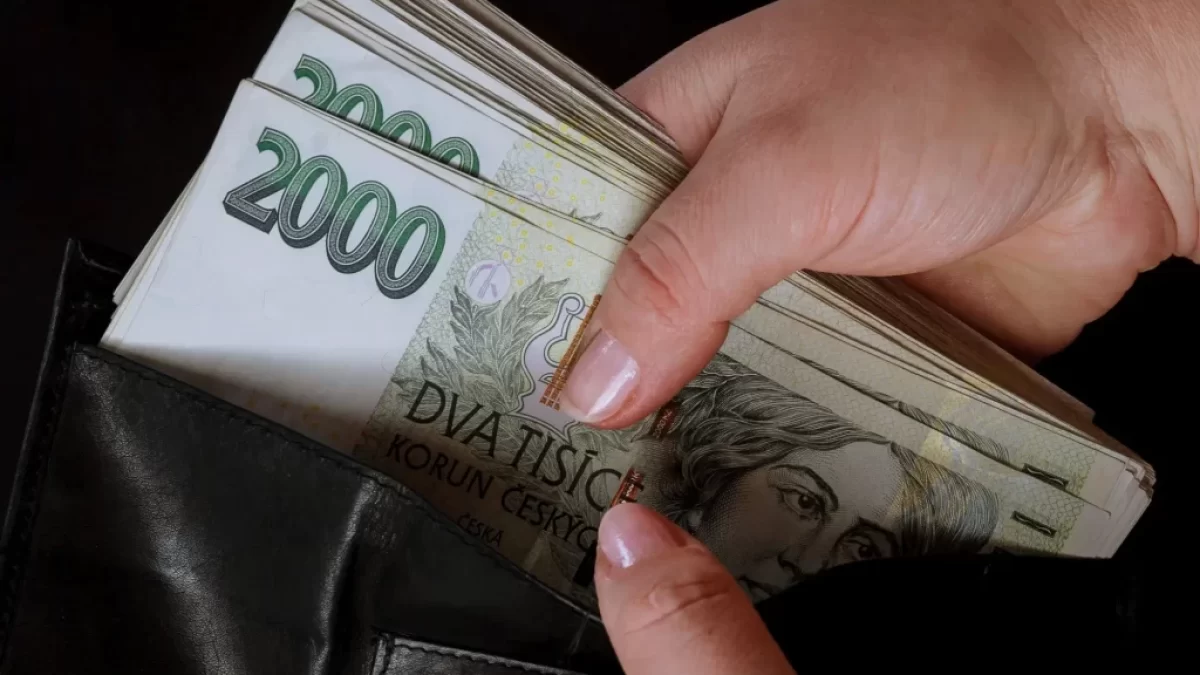 Detail ruky, která vytahuje větší svazek dvoutisícových bankovek z černé kožené peněženky.
