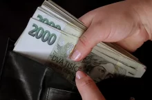 Detail ruky, která vytahuje větší svazek dvoutisícových bankovek z černé kožené peněženky.