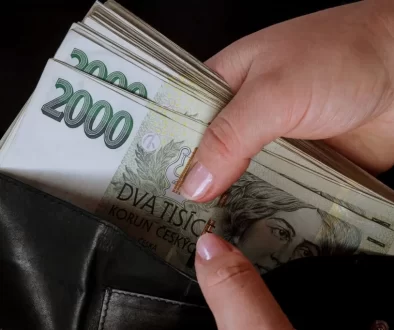 Detail ruky, která vytahuje větší svazek dvoutisícových bankovek z černé kožené peněženky.